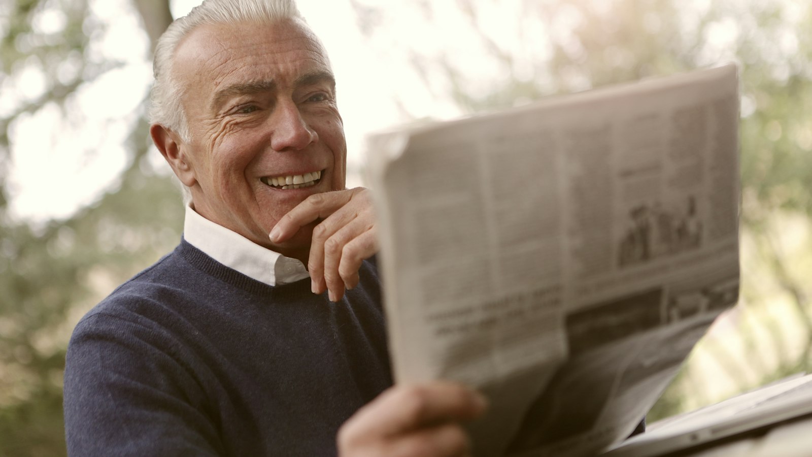 Homem idoso sorrindo enquanto lê o jornal