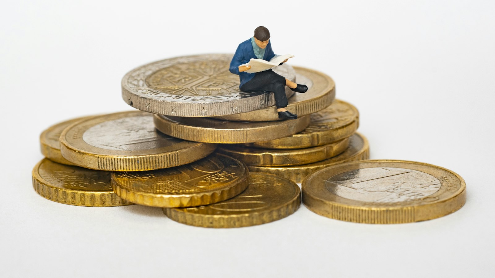 Miniatura de pessoa lendo jornal sobre pilha de moedas