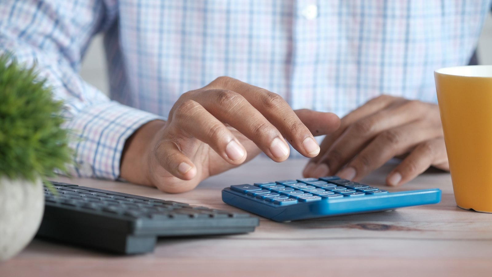 Mãos fazendo contas na calculadora sobre a mesa