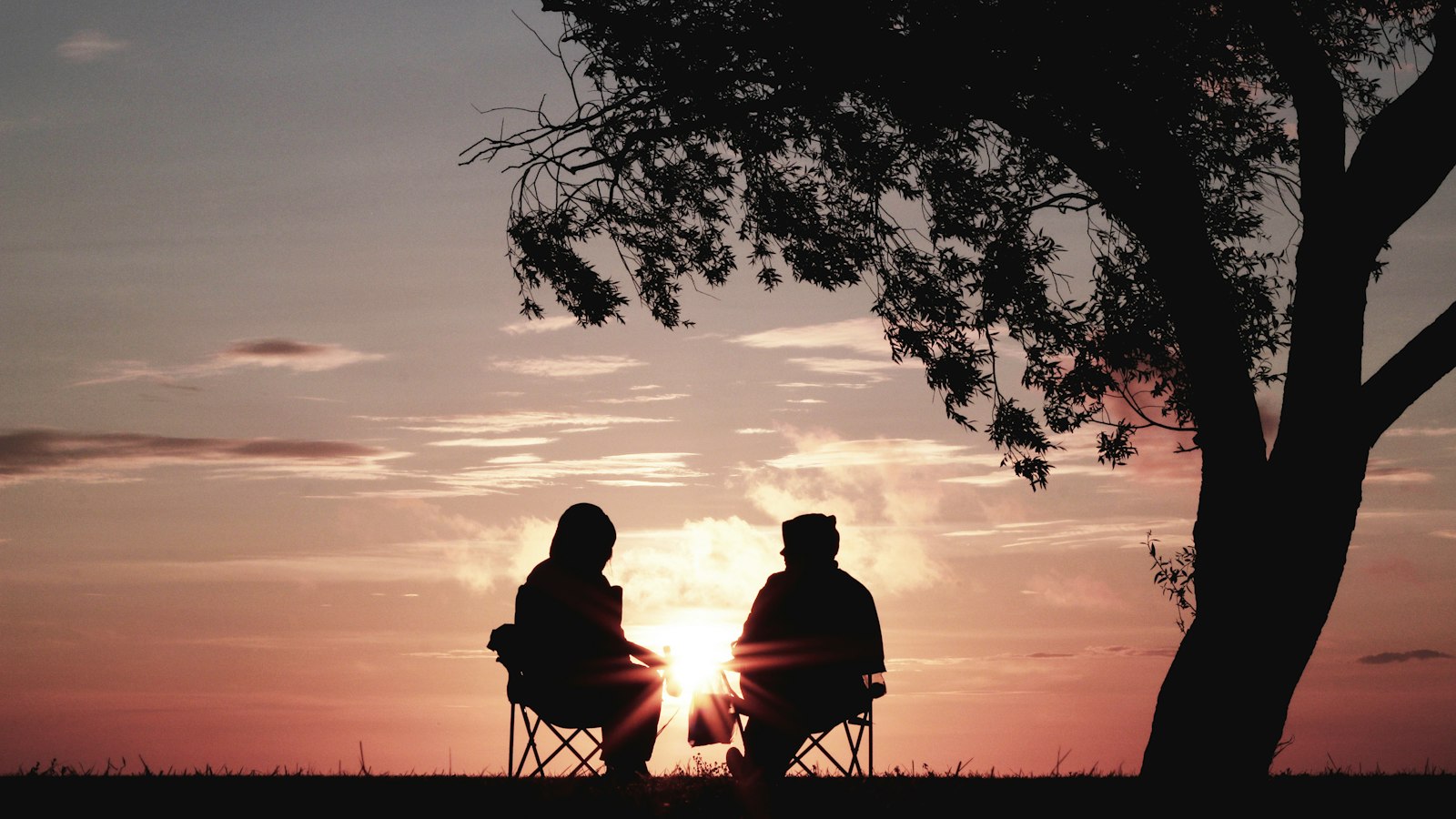 Casal sentado ao pôr do sol à sombra de uma árvore