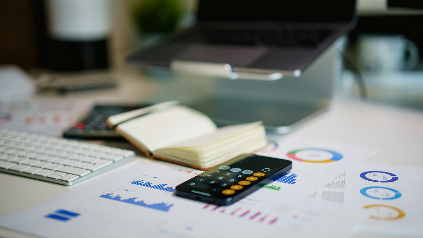 Mesa com celular, caderno e gráficos financeiros