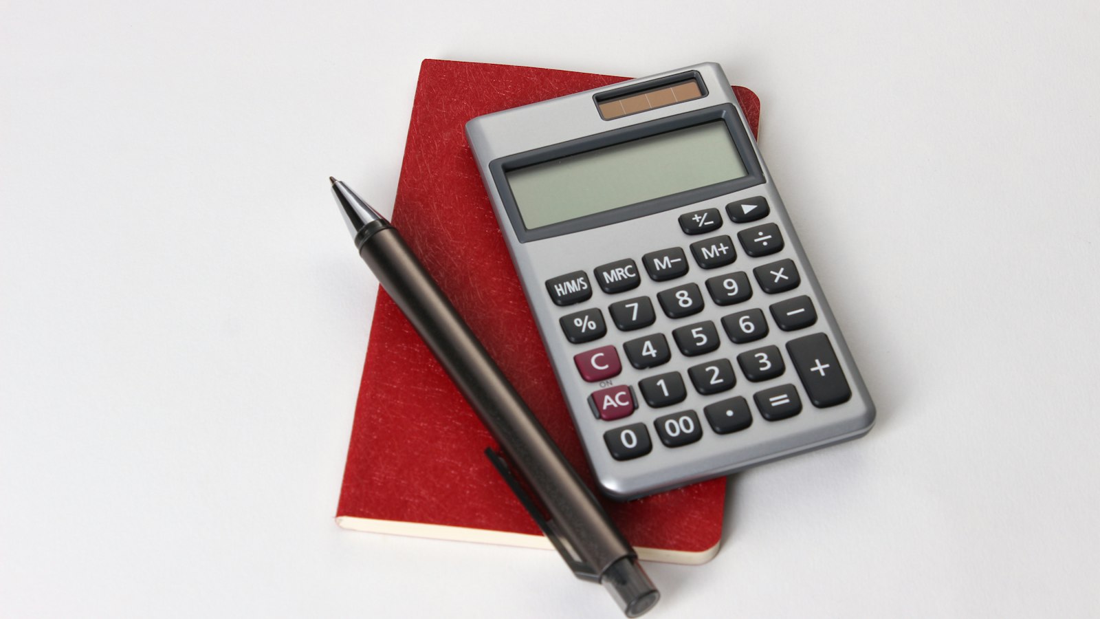 Calculadora e caneta sobre caderno vermelho