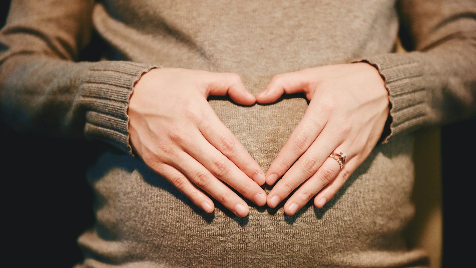Gestante fazendo um coração com as mãos sobre a barriga