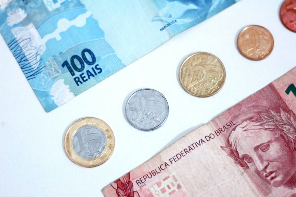 Cédulas de 100 e 10 reais e moedas de real sobre uma mesa branca