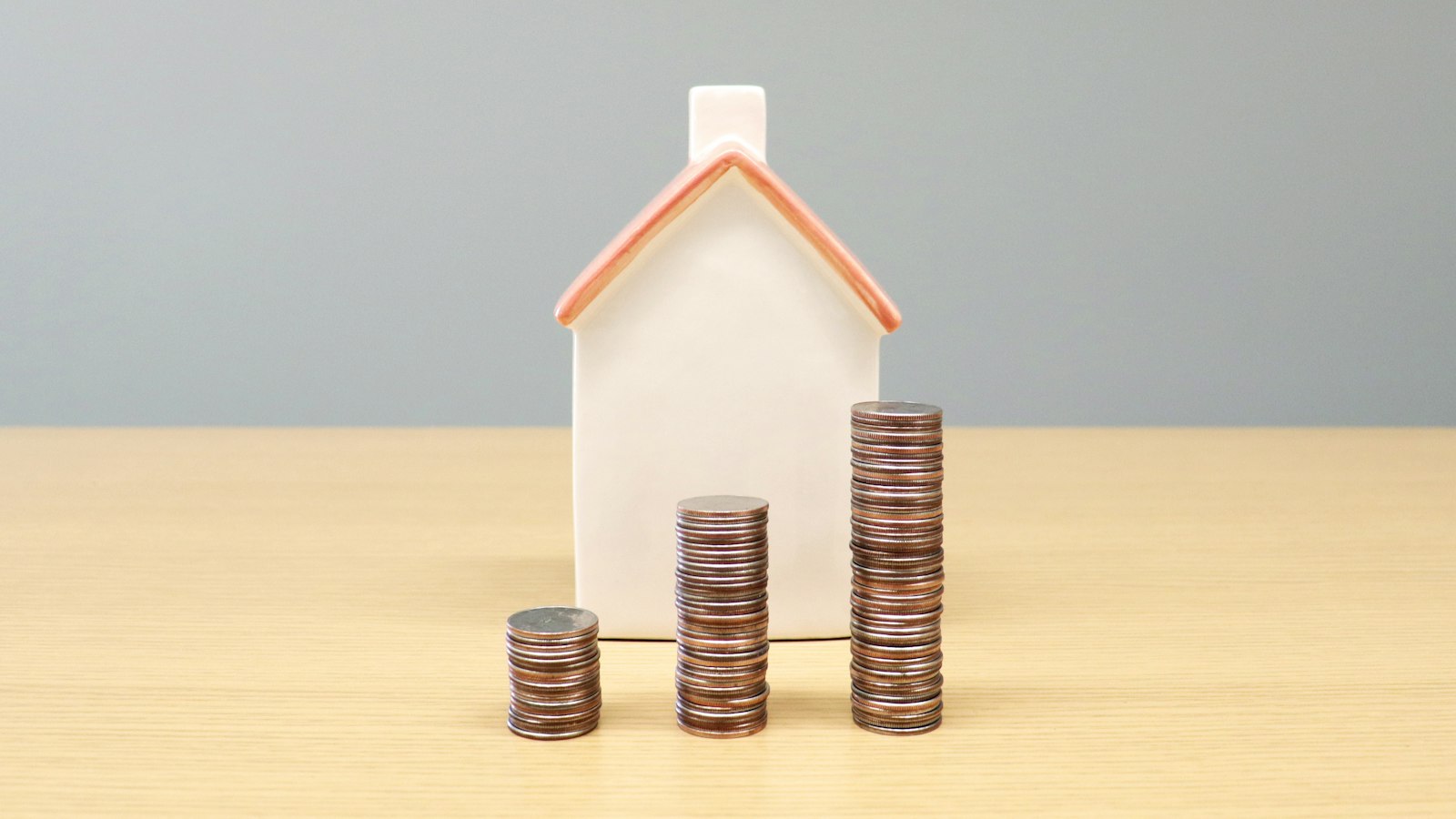 Miniatura de casa ao lado de pilhas de moedas