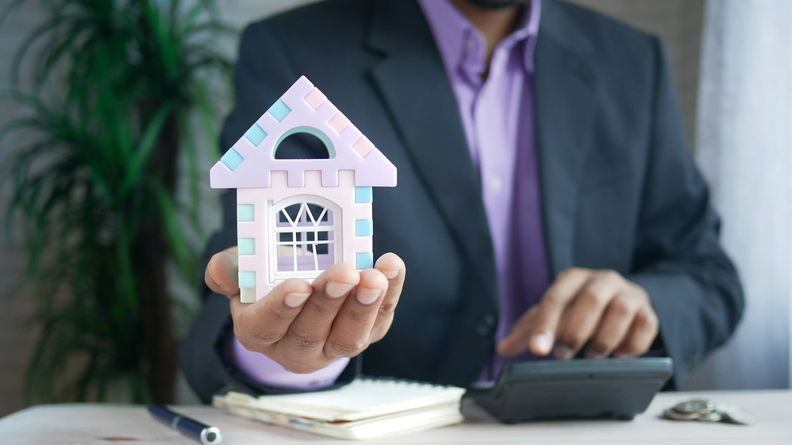 Homem segurando uma casa em miniatura ao lado da calculadora